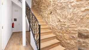 Una escalera con barandilla de metal negro, escalones de madera y pared de piedra.