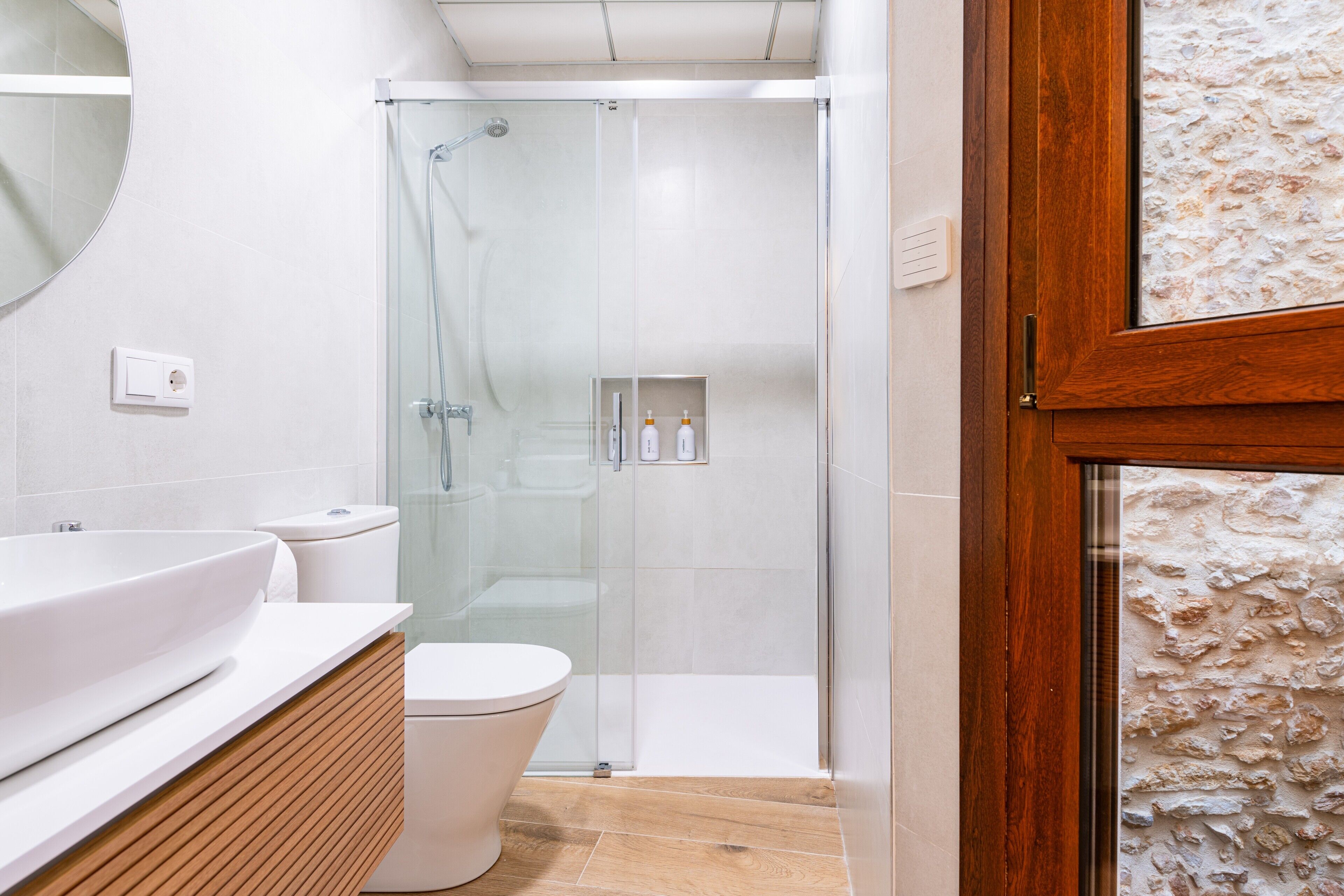 A modern bathroom with a glass-enclosed shower, a white sink, and a wooden vanity.
