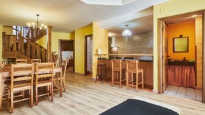 A wooden dining table with chairs, a kitchen with a tiled backsplash, and a staircase.