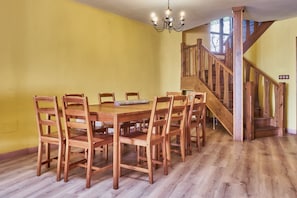 Ruokailutila, jossa on puinen pöytä ja tuolit, kattokruunu sekä puinen portaikko.