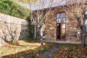 A stone building with a large window and a door, surrounded by trees and a stone wall.