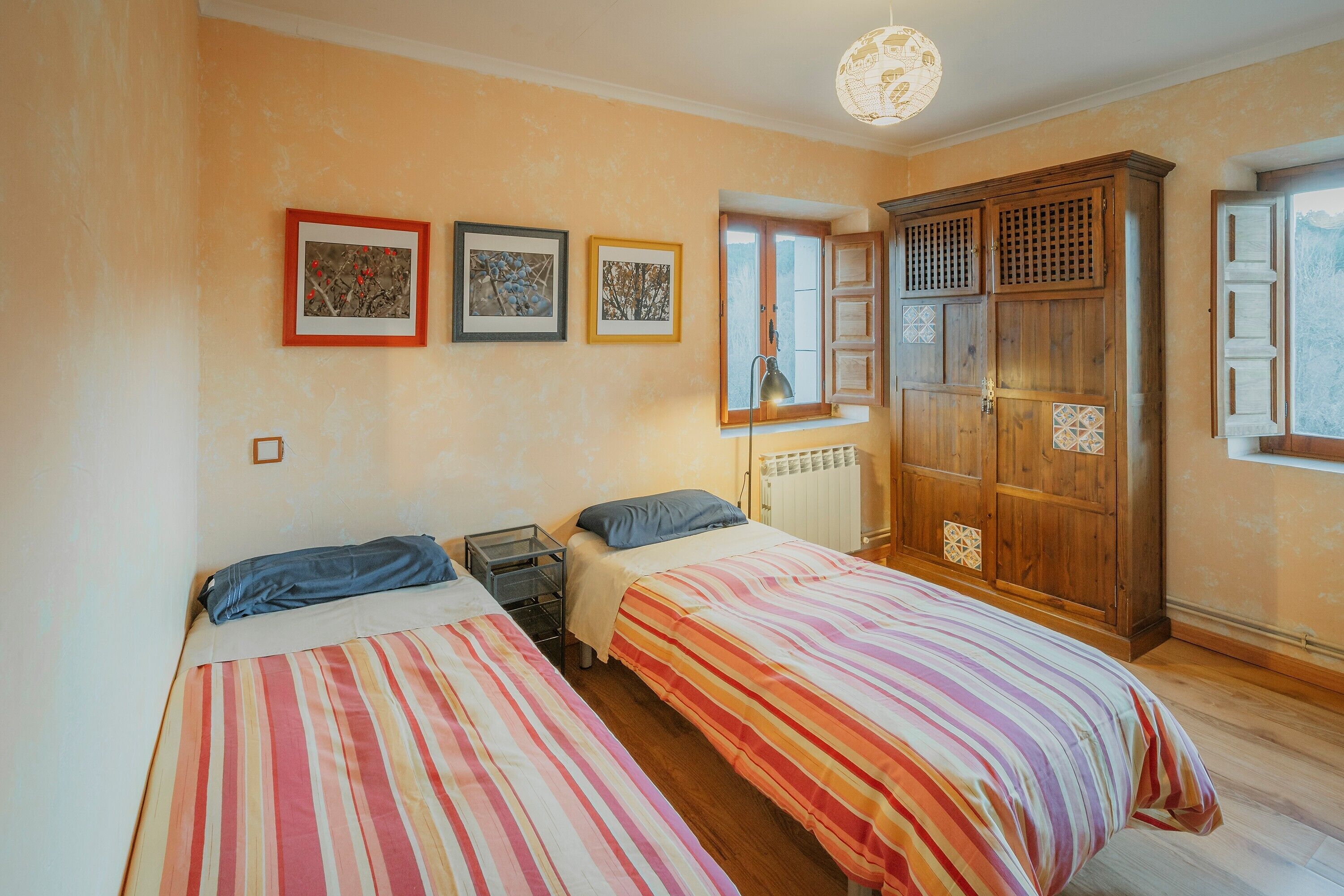 A room with two beds, a wooden wardrobe, a radiator, and framed artwork on the wall.