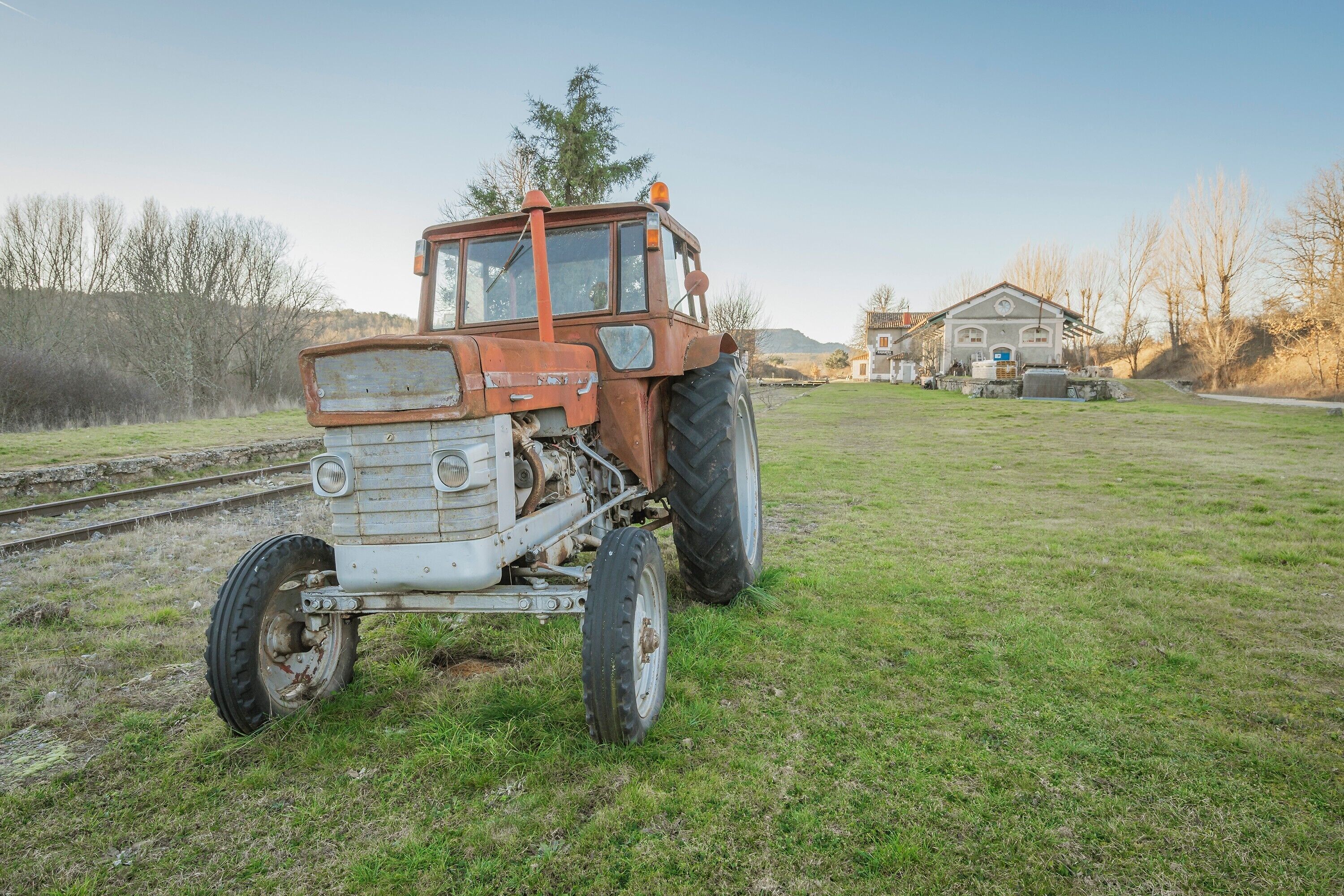 Un tractor en un campo de hierba con una casa al fondo.