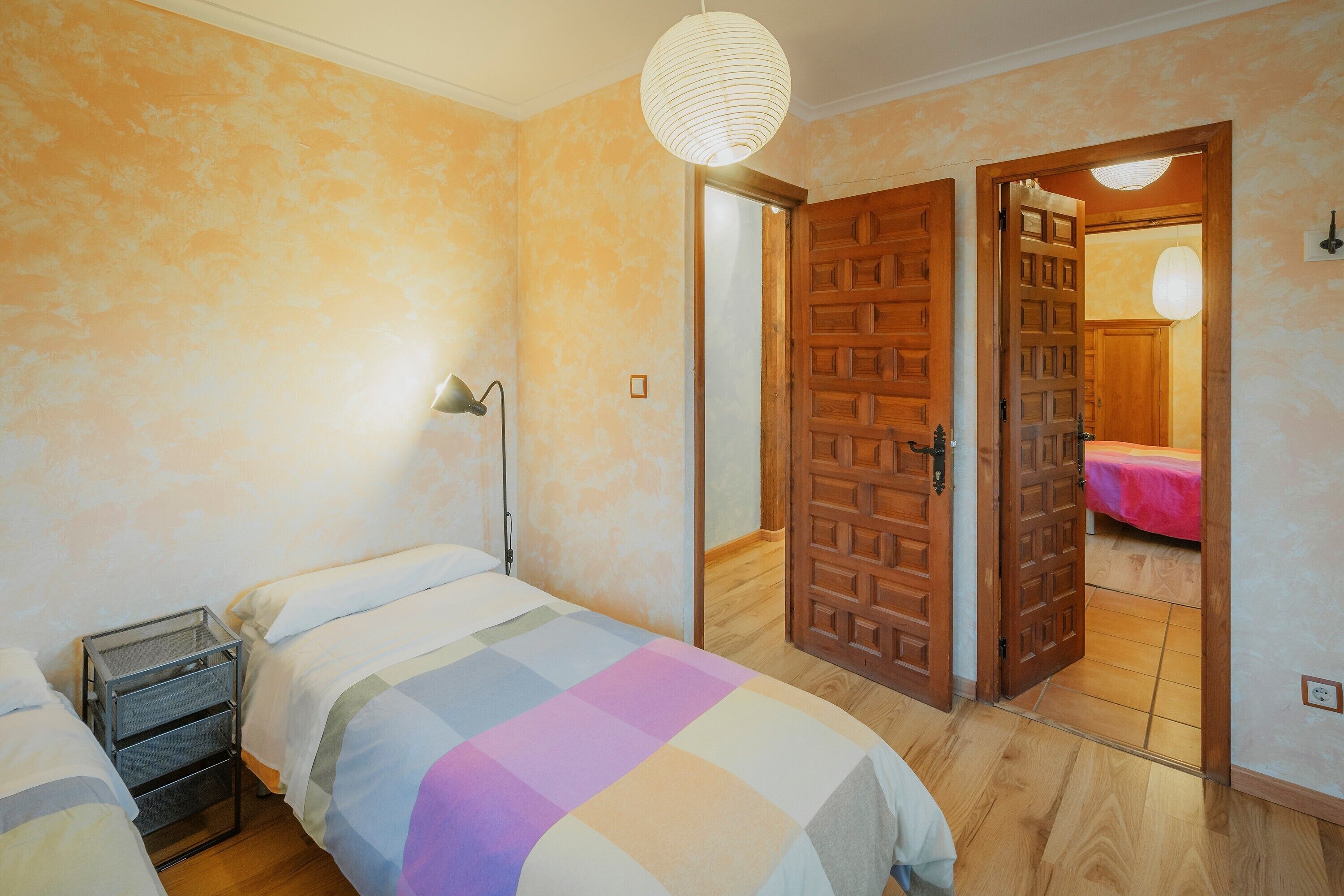 Un dormitorio con dos camas, una mesita de noche, una lámpara y una puerta de madera que da a otra habitación.
