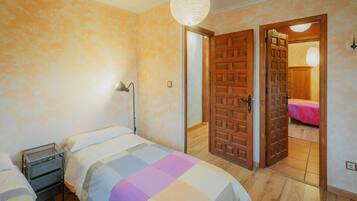 Un dormitorio con dos camas, una mesita de noche, una lámpara y una puerta de madera que da a otra habitación.