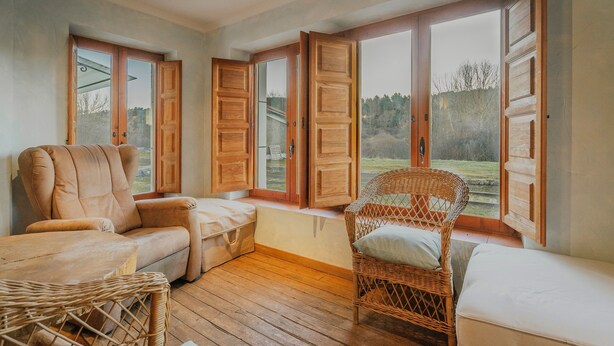 Ein gemütliches Zimmer mit einer Couch, einem Korbsessel und einem Fenster mit Holzhörnern.