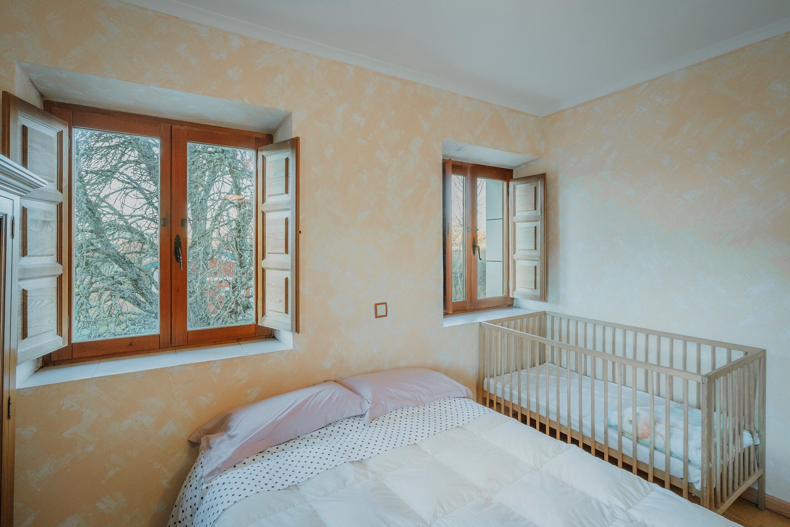 Un dormitorio con una cuna, una ventana con contraventanas y un papel tapiz estampado.