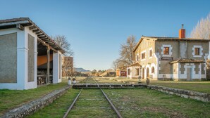 Ein ländlicher Bahnhof mit freier Strecke, einem Gebäude mit der Aufschrift 'RABANERA' und einer grünen Wiese.