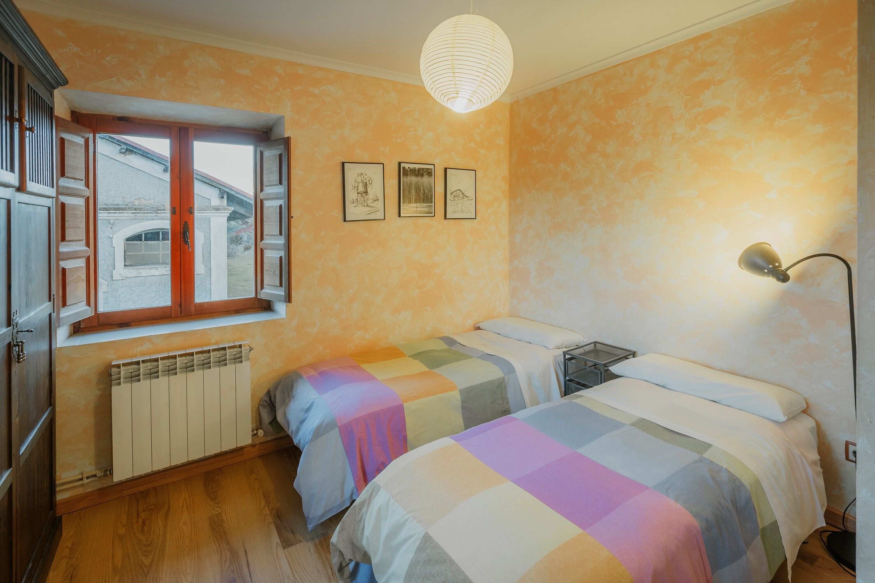 Un dormitorio con dos camas, un radiador, una ventana y una lámpara fijada a la pared.
