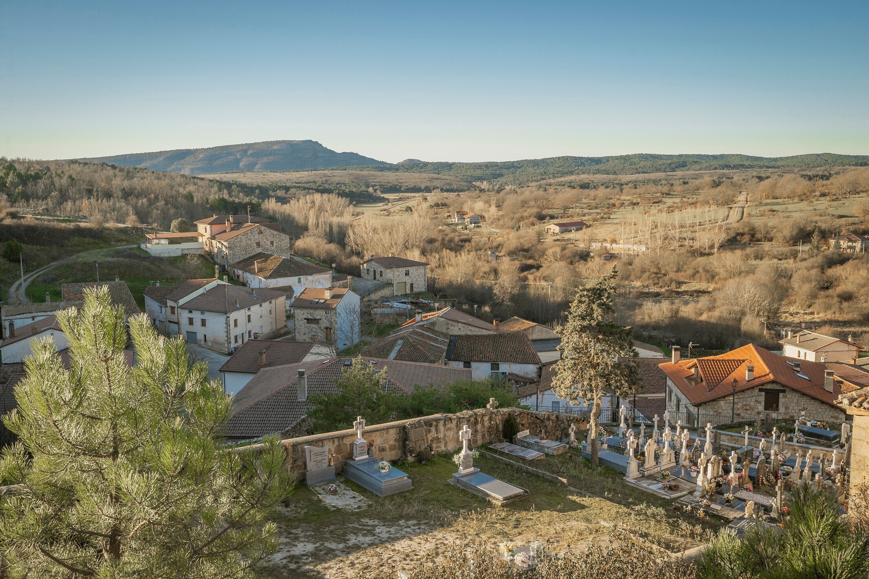 Un pueblo rural con casas de piedra, un cementerio y un paisaje montañoso al fondo.