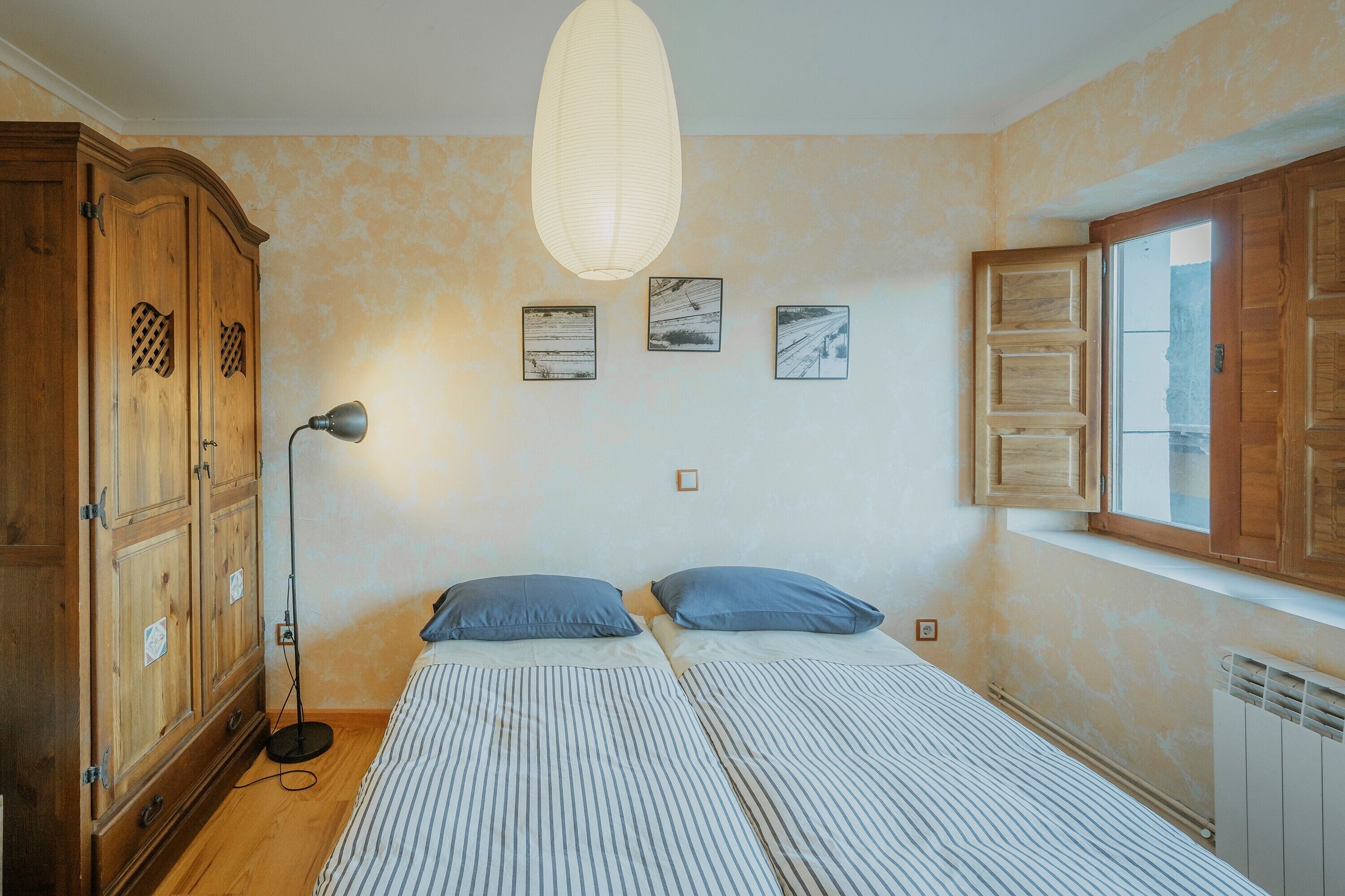 A bedroom with a bed, a wardrobe, a floor lamp, and three framed pictures on the wall.