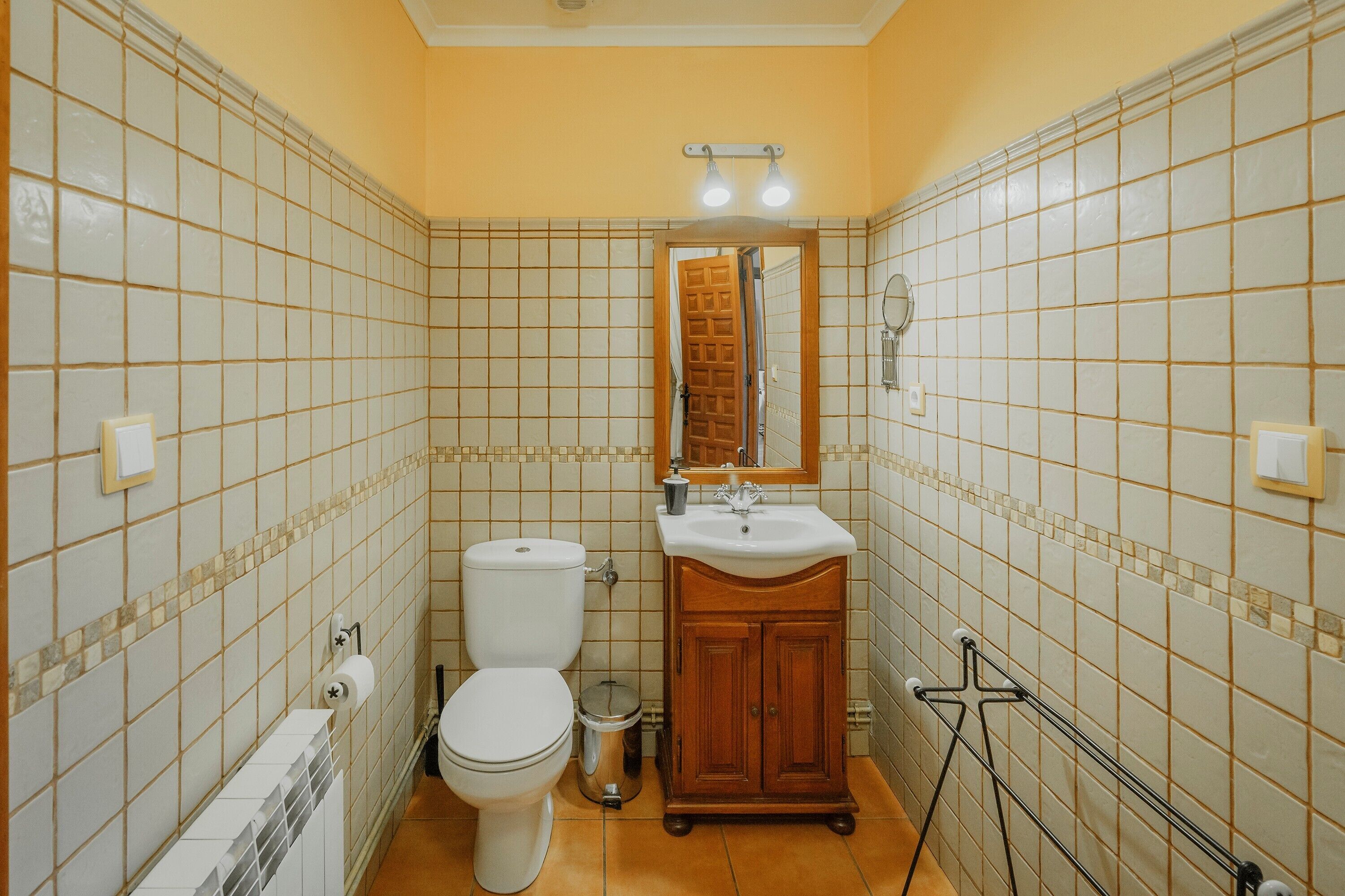 Un baño con inodoro, lavamanos, espejo y paredes con azulejos.
