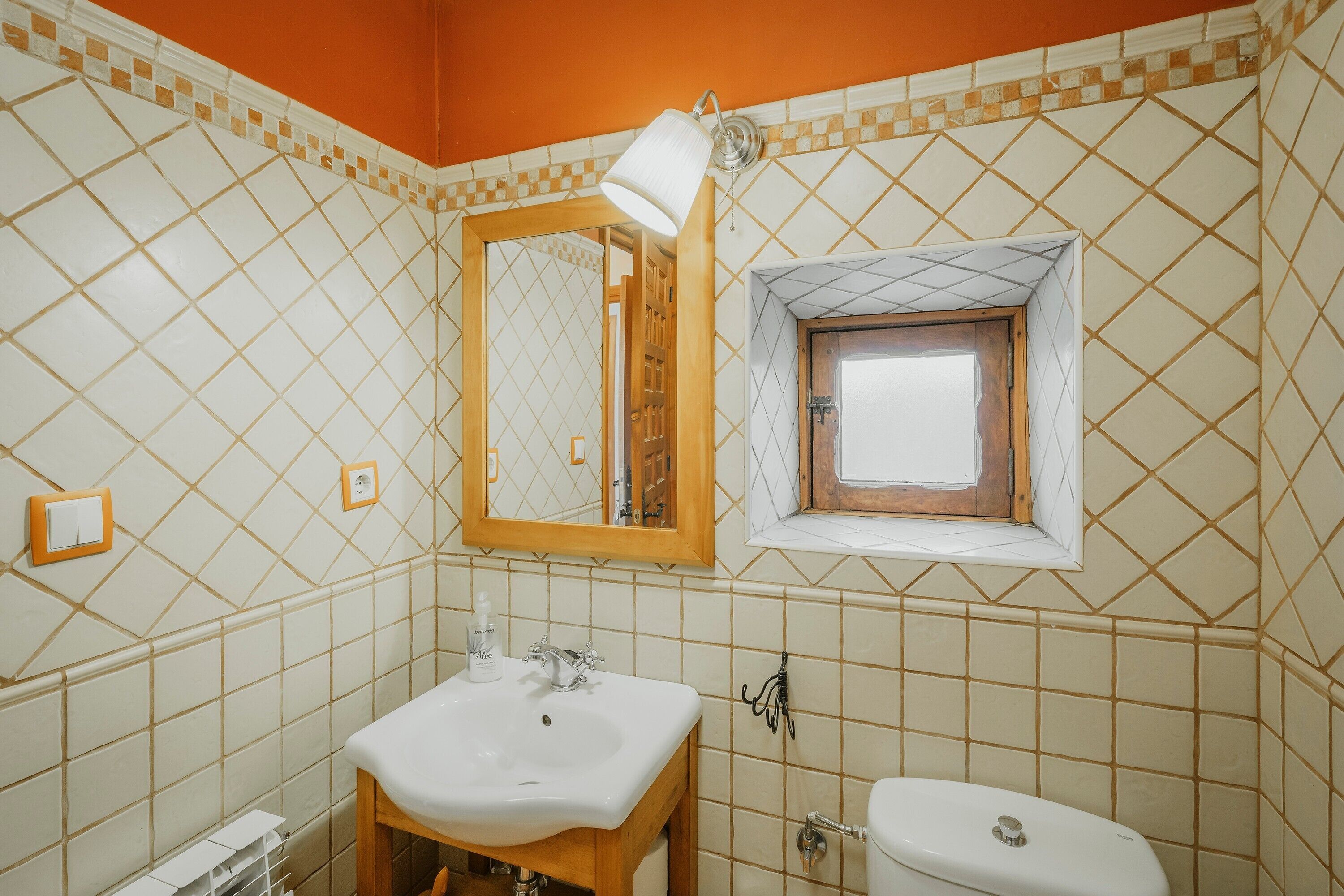 Un baño con piso de baldosas, un lavamanos, un inodoro, un espejo y una ventana.