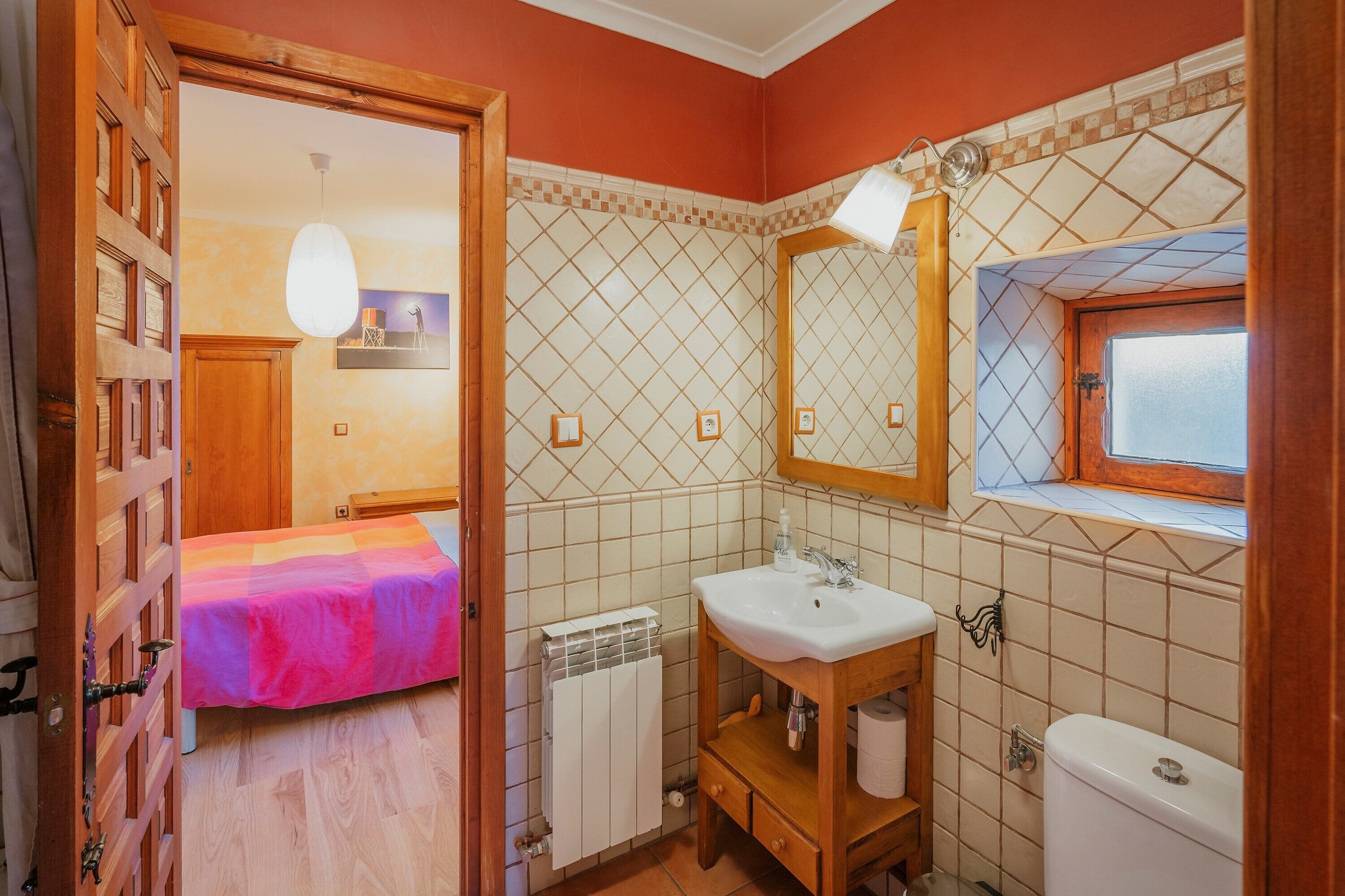 A bathroom with a bed, a sink, a toilet, and a window.