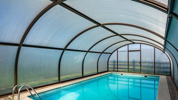 Piscina com teto de vidro, água cristalina e escada de metal.