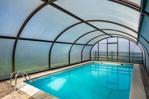 A swimming pool with a glass ceiling, clear pool water, and a metal ladder.
