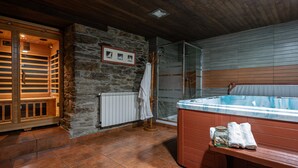 Uma área de spa com parede de pedra, bancos de madeira, box de chuveiro em vidro e banheira de hidromassagem.