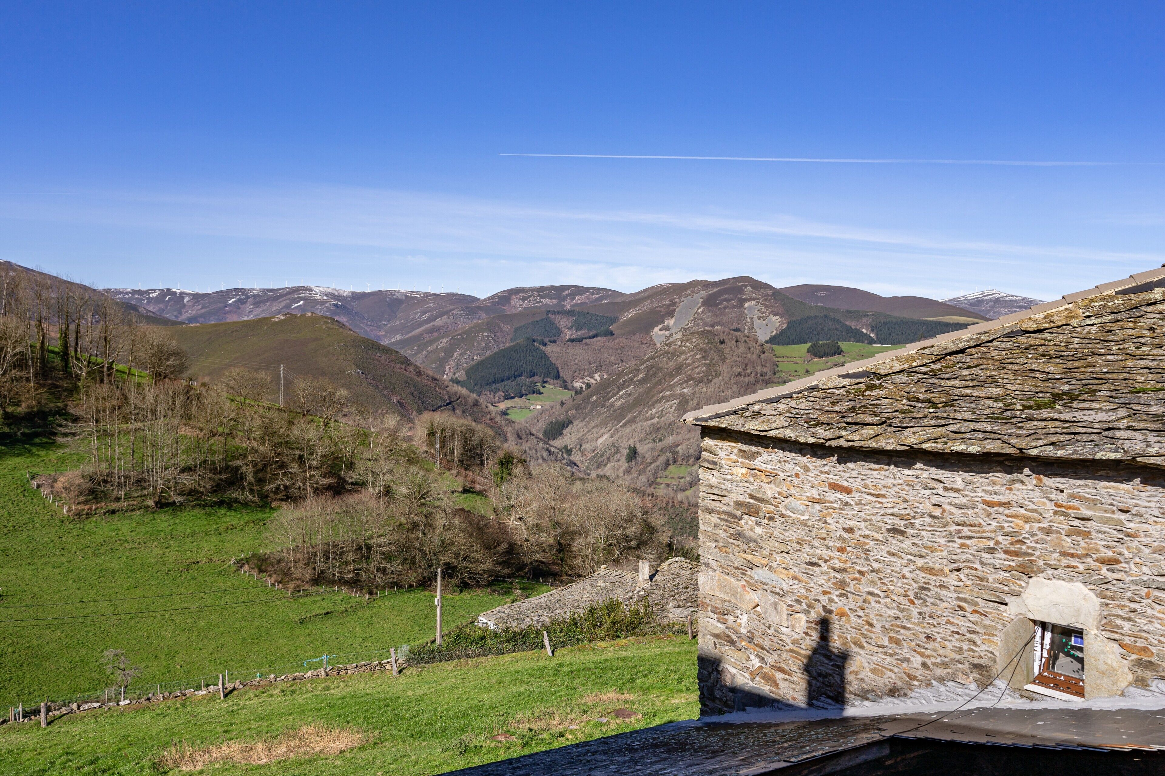Um edifício de pedra com uma pequena janela, rodeado por um vale verde e montanhas.