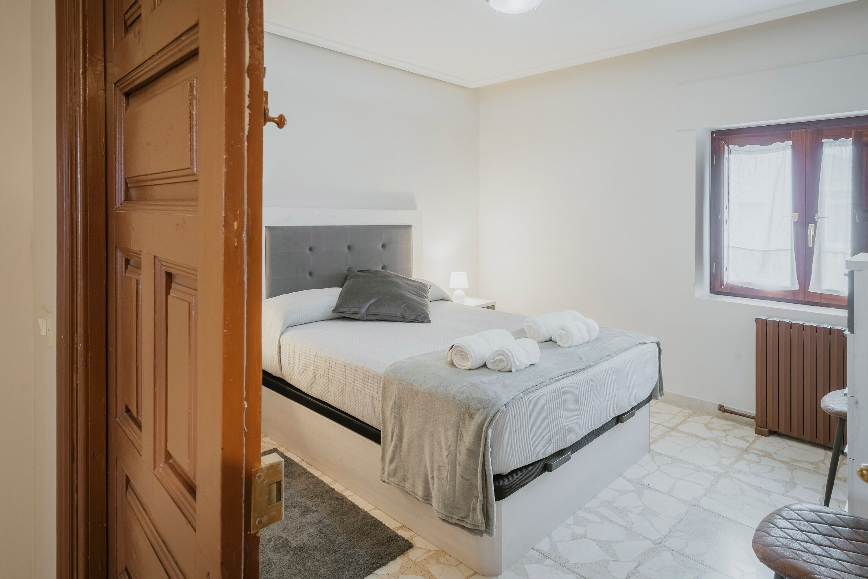 Un dormitorio con cama, ventana, radiador y puerta.