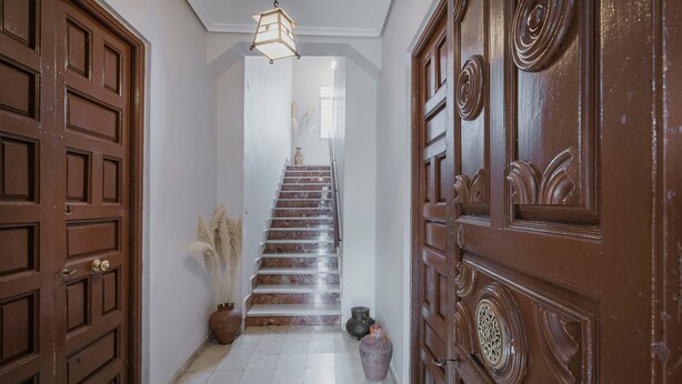 Un corridoio con una scala, porte in legno e un lampadario.