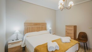 Una camera d'albergo con un letto, un comodino con una lampada, una cassettiera in legno e una sedia.