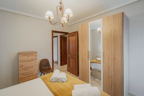 A bedroom with a bed, a wooden dresser, a chair, a wardrobe, and a bathroom visible through an open door.