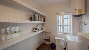 A laundry room with a washing machine, dryer, and a water heater. There are shelves with bottles and a chair.