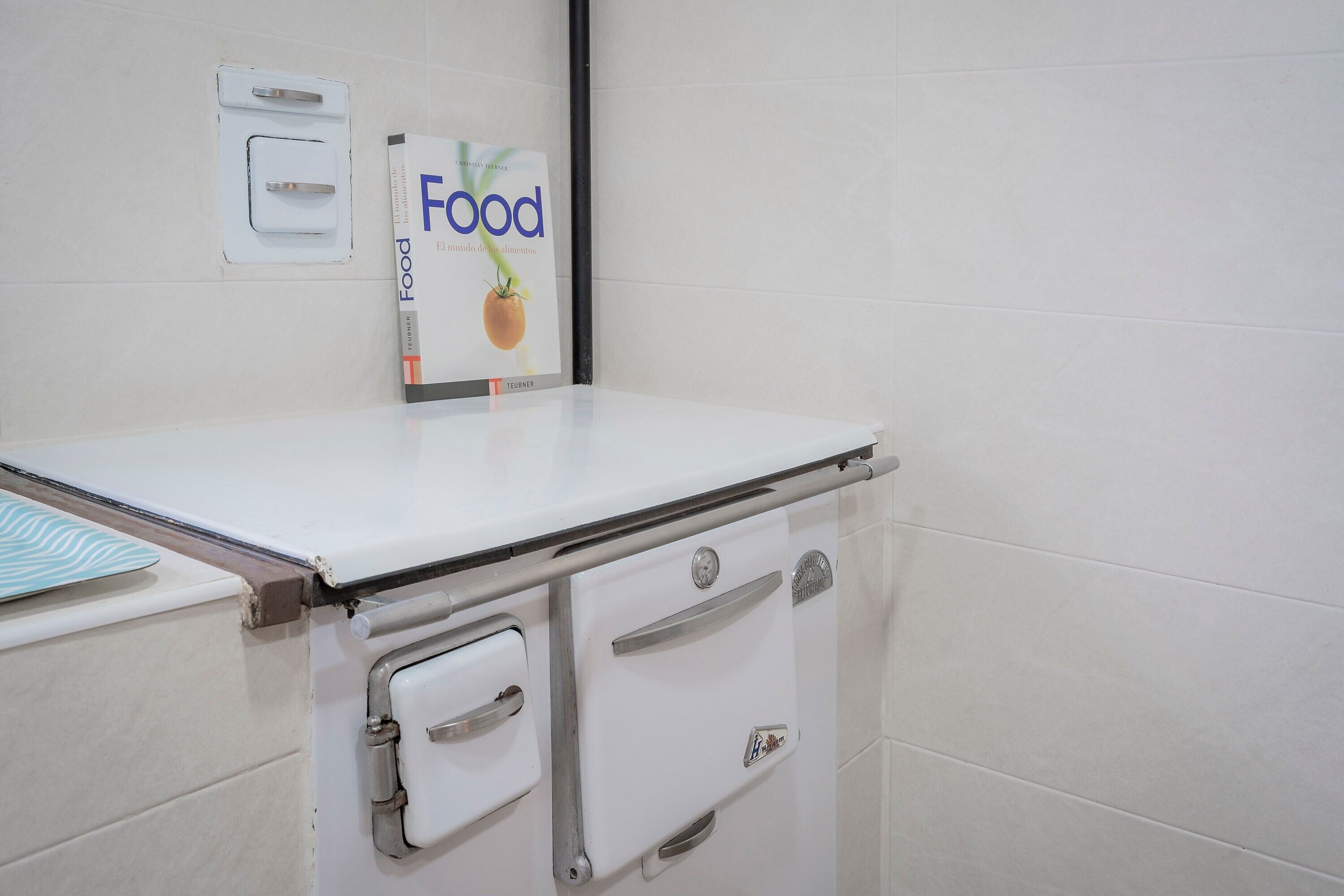 Una cocina con armarios blancos, una encimera blanca y un libro titulado 'Food' en la pared.