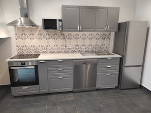 A modern kitchen with grey cabinetry, a built-in microwave, a dishwasher, and a stainless steel refrigerator.