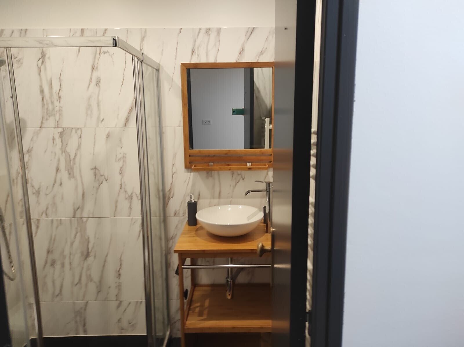 Une salle de bain avec une douche à parois de verre, un meuble-lavabo en bois avec un évier blanc et un miroir au-dessus de l’évier.
