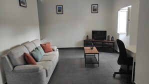 Ein modernes Wohnzimmer mit einem grauen Sofa, einem Couchtisch, einem Fernseher und einem schwarzen Bürostuhl.