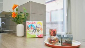 A kitchen counter with a vase of flowers, a board game, and a glass jar. - Charming Stoke-on-trent House Getaway (Stoke-on-Trent)