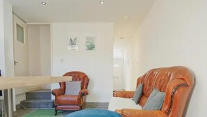 A room with a brown leather chair, a blue table, and a staircase leading to another room. - Charming Stoke-on-trent House Getaway (Stoke-on-Trent)