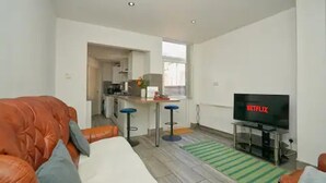 A modern living room with a leather sofa, a TV displaying 'NETFLIX', and a kitchen in the background. - Charming Stoke-on-trent House Getaway (Stoke-on-Trent)