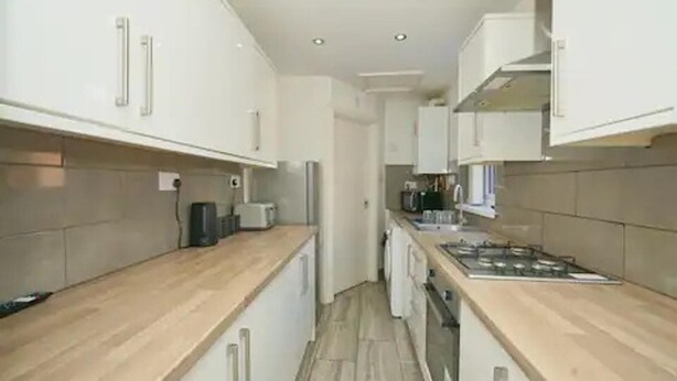 A narrow kitchen with white cabinets, a wooden countertop, and a stove. - Charming Stoke-on-trent House Getaway (Stoke-on-Trent)
