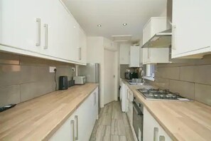 A narrow kitchen with white cabinets, a wooden countertop, and a stove. - Charming Stoke-on-trent House Getaway (Stoke-on-Trent)