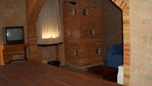 Quarto com lareira de tijolos, televisão sobre suporte de madeira e uma cadeira azul.