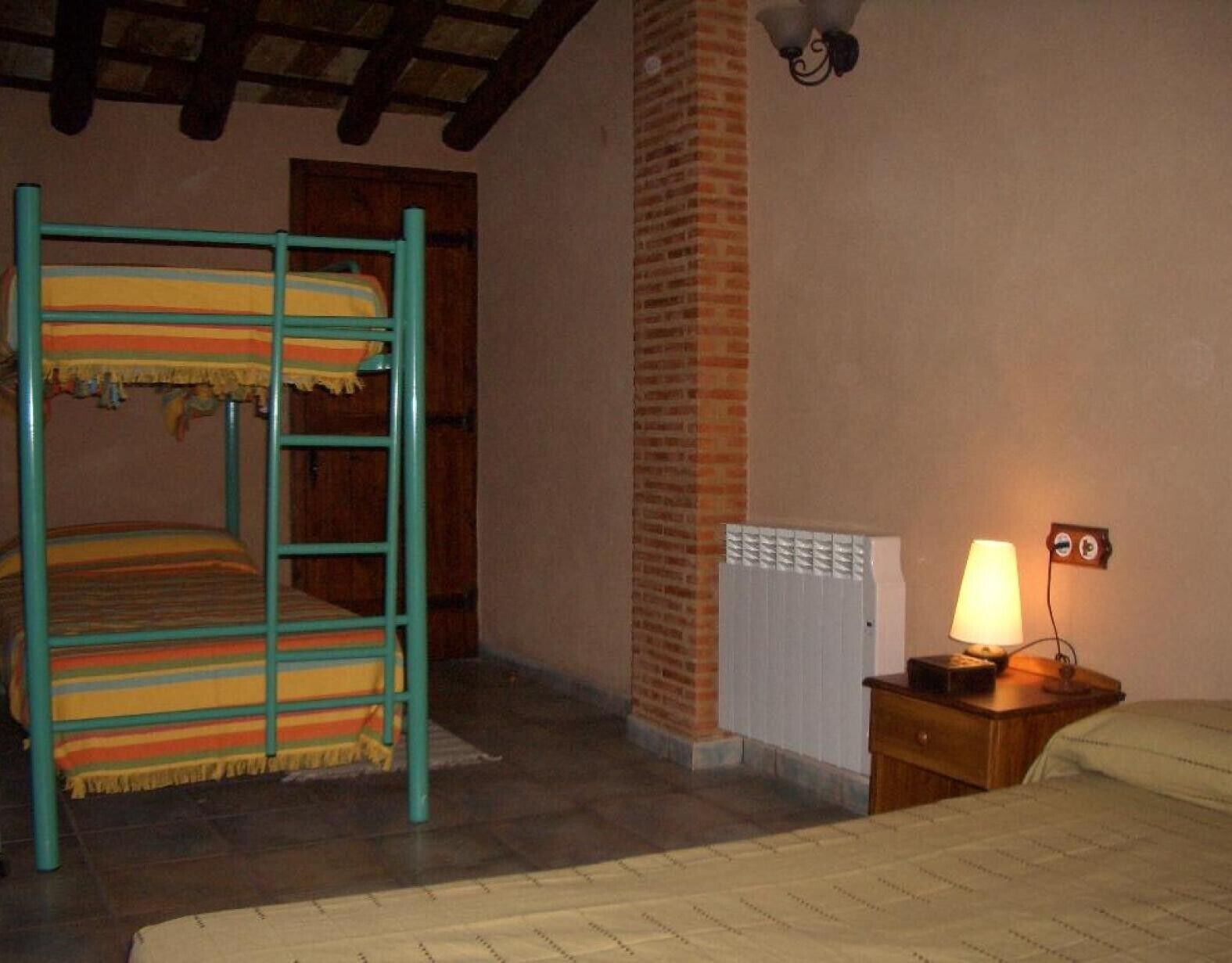 Una habitación con una cama litera, una chimenea de ladrillo, una mesita de noche con lámpara y un radiador.