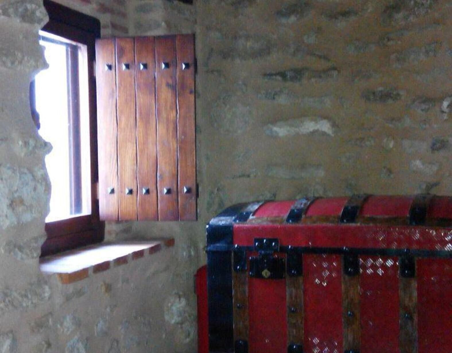 A room with a wooden wardrobe, a small window, and a red suitcase.