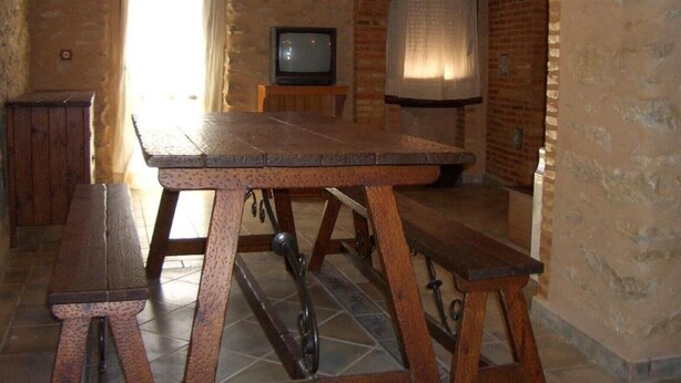 Um quarto rústico com uma mesa de madeira, bancos, uma televisão e uma parede de tijolos.