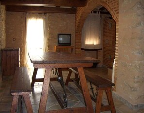 A rustic room with a wooden table, benches, a television, and a brick wall. - Country House 'Casa Gimeno' with Mountain View, Wi-Fi and Air Conditioning (Bocairent)