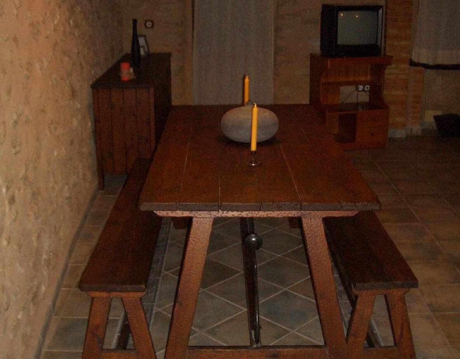 Una mesa de madera con bancos, un televisor sobre un mueble bajo y una vela sobre la mesa.