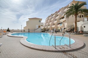 Une piscine avec une terrasse carrelée, un palmier et un bâtiment doté de balcons en arrière-plan.