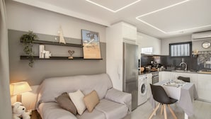 A modern living room with a sofa, a dining table, and a kitchen area with appliances.