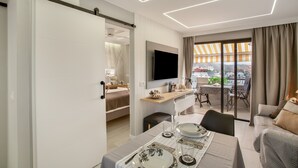 A modern hotel room with a dining area, a TV, and a balcony with a city view.