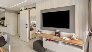 A modern living room with a flat-screen TV mounted on the wall, a wooden coffee table, a seating area with a chair, and a sliding door closet.