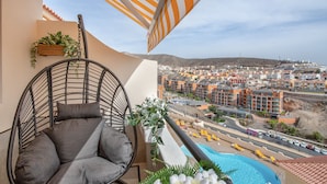 A balcony with a hanging chair, a small pool, and a view of a coastal town.