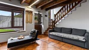 Una habitación con sofá, banca, escalera y ventana con vista a un jardín.