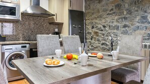 Una cocina con pared de piedra, horno empotrado y comedor con sillas y una mesa dispuesta para el desayuno.