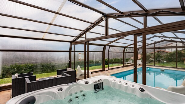 Un jacuzzi dentro de un invernadero, con una piscina en el exterior.